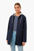 A woman wears a Saint James navy waterproof raincoat over a striped shirt and light blue jeans, showcasing a classic nautical look.