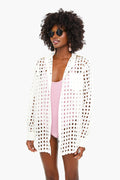 A woman stands confidently in Solid & Striped sunglasses, a light pink swimsuit, and a white mesh beach coverup featuring large circular cutouts.