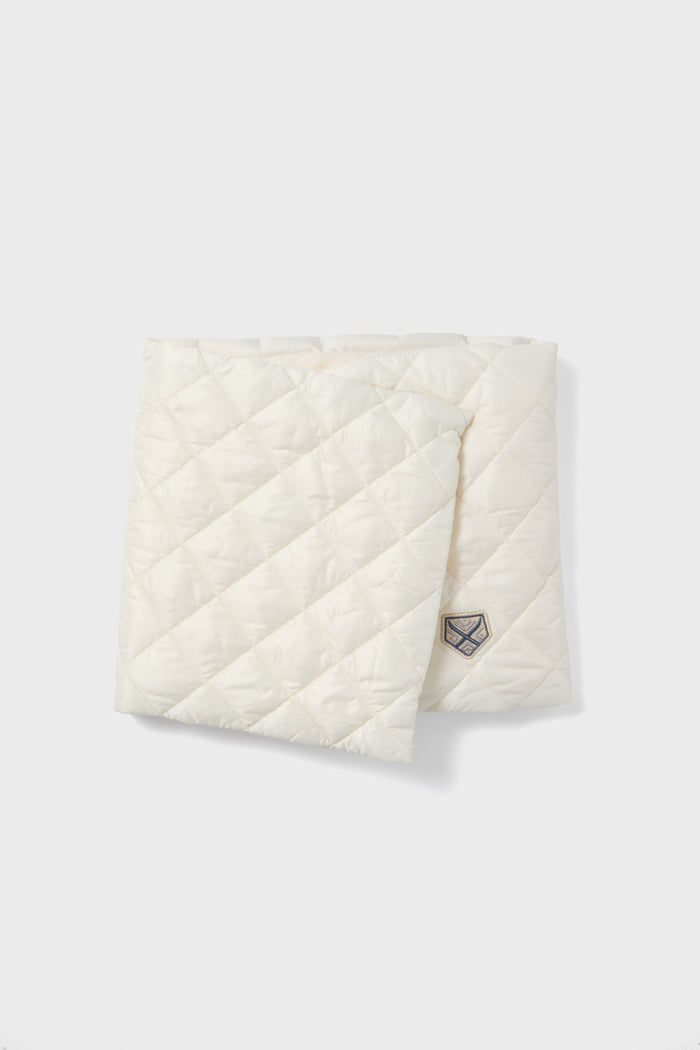 The Powder Puff Collection features a folded, quilted white scarf with a diamond pattern and stitched logo patch, crafted from sustainable materials for a luxurious winter accessory.