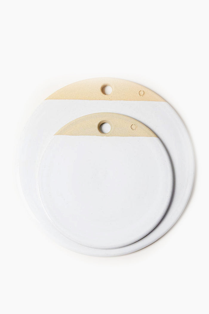 Two round ceramic objects by Farmhouse Pottery, Inc., crafted from durable stoneware in white and beige color blocks, each with a top-edge hole, stacked asymmetrically in signature Vermont farmhouse style.