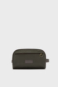 The Barbour Olive Wax Washbag is a rectangular, dark green men’s toiletry bag with a zippered front pocket, leather patch, gold zipper pull, and side handle.