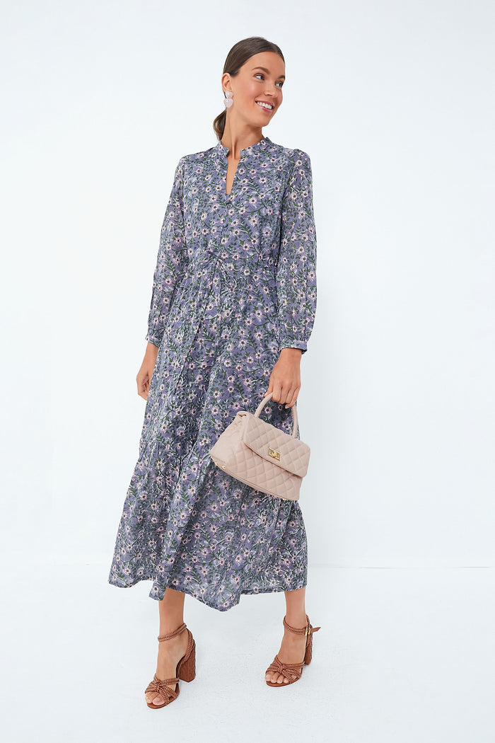 A woman wears a Love Tomas by Emerson Fry long-sleeved floral dress in organic cotton, holding a beige quilted handbag and wearing brown heeled sandals.