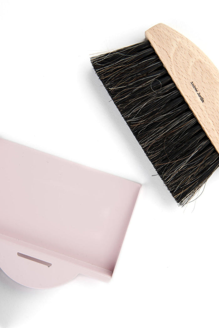 An Andree Jardin small brush with black bristles and a wooden handle is beside a pale pink plastic dust pan and brush, all made in France.