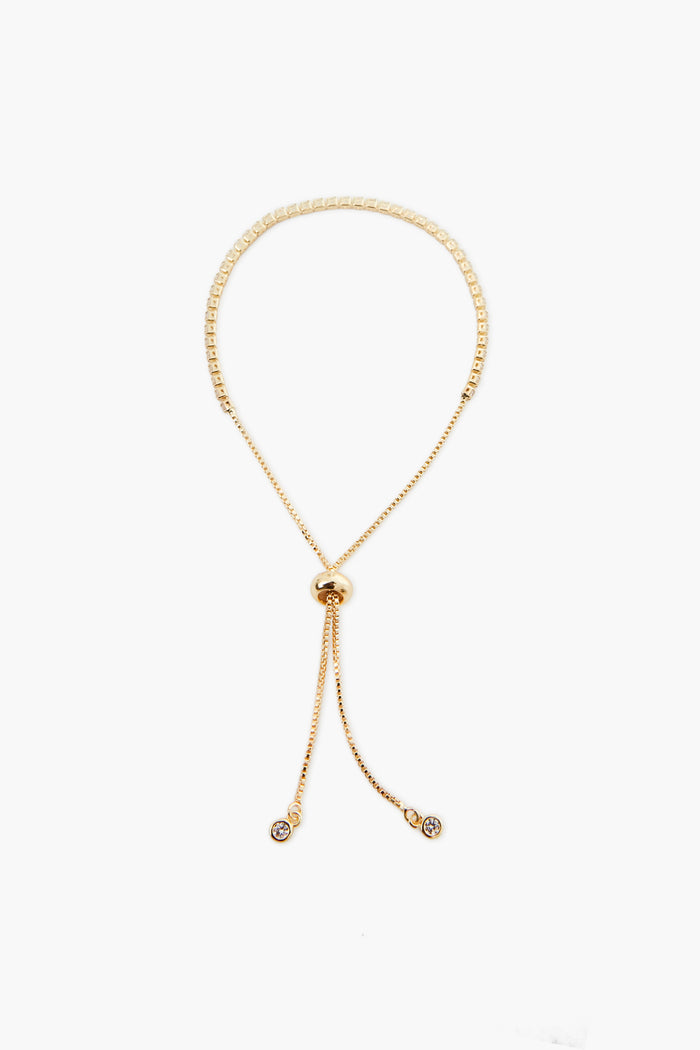 A gold adjustable necklace from Petit Moments, a woman-owned Los Angeles brand, features a round sliding clasp and two dangling ends, each with a small circular charm.