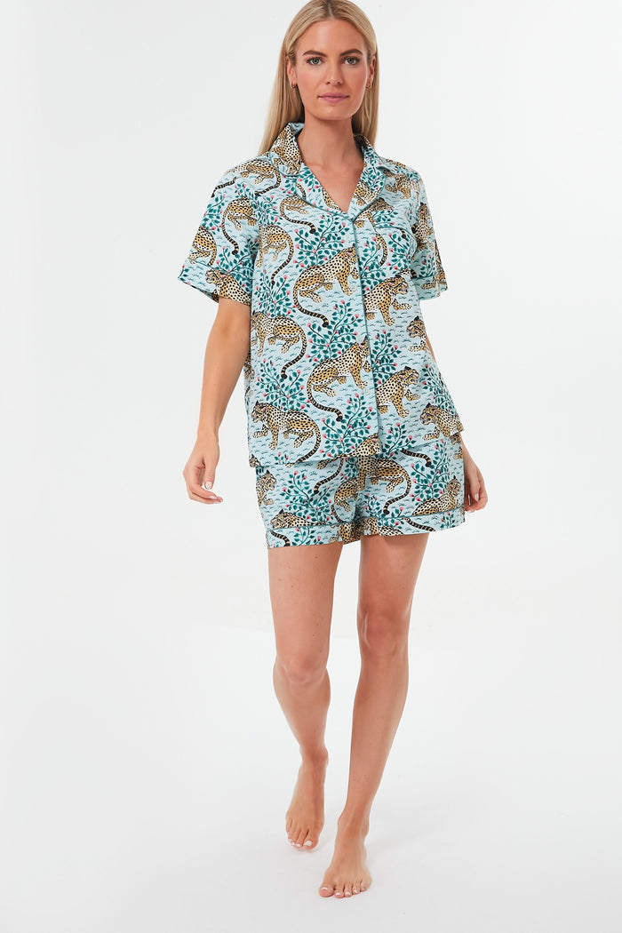 A woman stands barefoot wearing the Printfresh x Tuckernuck short-sleeve button-up shirt and shorts, a blue leopard print pajama set—an ideal choice for women's sleepwear.