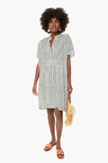 A woman wears a knee-length, loose, short-sleeved Emerson Caftan by Love Tomas by Emerson Fry, crafted from hand block printed organic cotton, styled with tan sandals, statement earrings, and a woven fringe handbag.