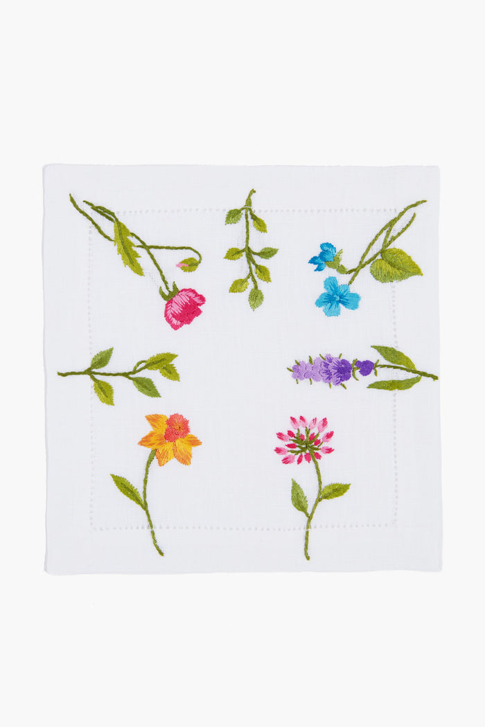 Tuckernuck Home’s white linen napkin features hand embroidery with colorful flowers and green stems arranged around the center.