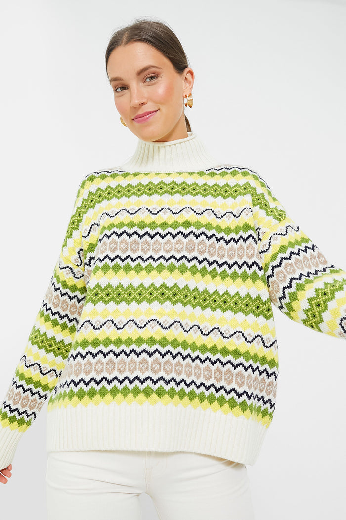 A woman wears a Barbour women’s wool sweater styled as a white turtleneck, featuring green, yellow, and black geometric Fair Isle knit patterns.