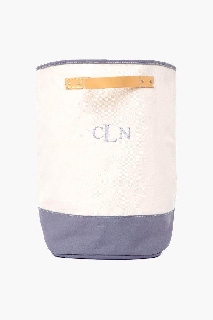 A CB Station canvas hamper made from natural materials, featuring a blue base, cream upper section, tan handle, and "CLN" embroidered on the front.