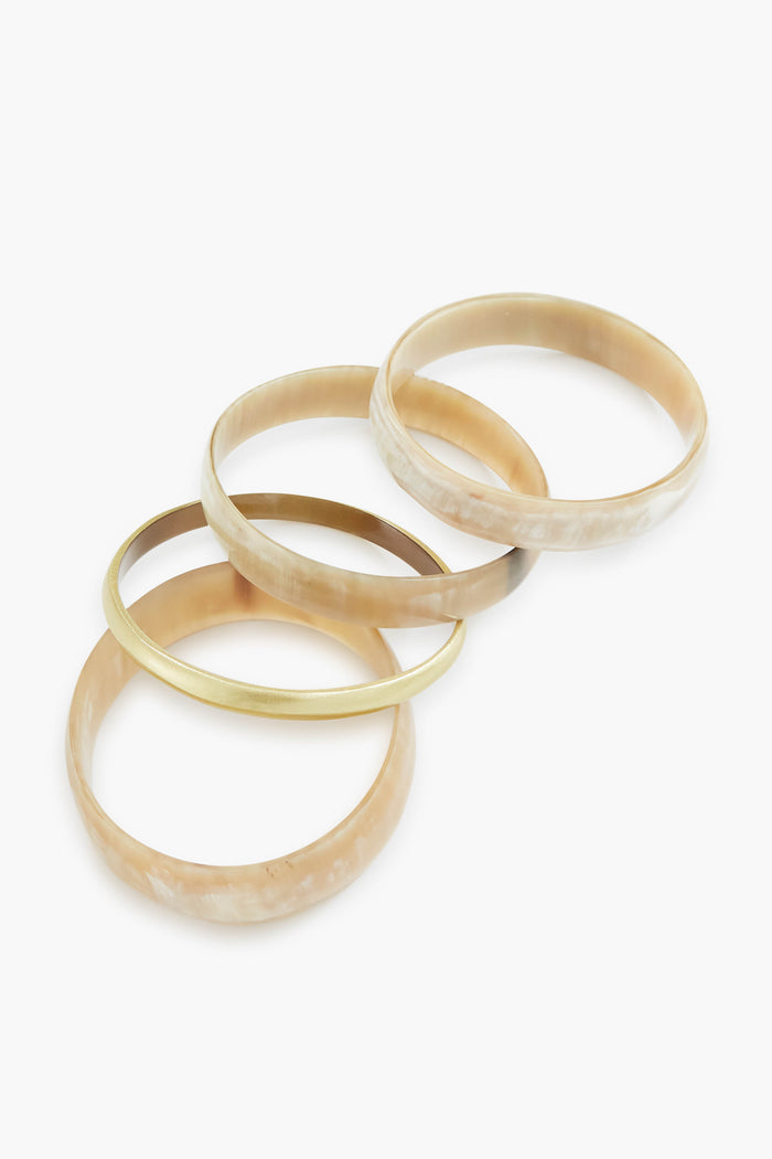 Four round bangles from Sunshine Tienda's lightweight set are arranged on a white surface—three feature a beige marbled pattern, and one has a plain gold finish.
