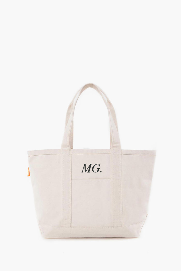 This cream-colored canvas tote by CB Station features two handles and the initials MG. printed on the front pocket.