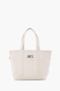 This cream-colored canvas tote by CB Station features two handles and the initials MG. printed on the front pocket.