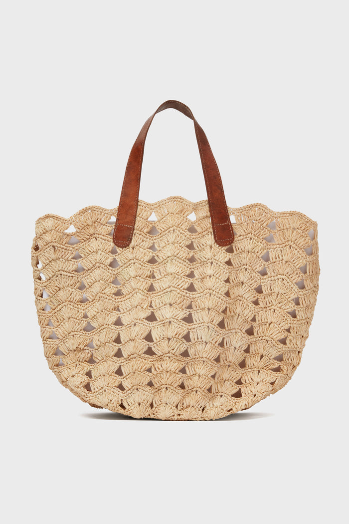 The Mar y Sol woven straw tote bag features a scalloped edge and two brown leather shoulder straps, making it a stylish and sustainable choice for the beach.