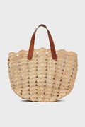The Mar y Sol woven straw tote bag features a scalloped edge and two brown leather shoulder straps, making it a stylish and sustainable choice for the beach.