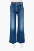 A pair of high-rise, wide-leg blue jeans with a faded wash by MOTHER, shown on a mannequin wearing white shoes.