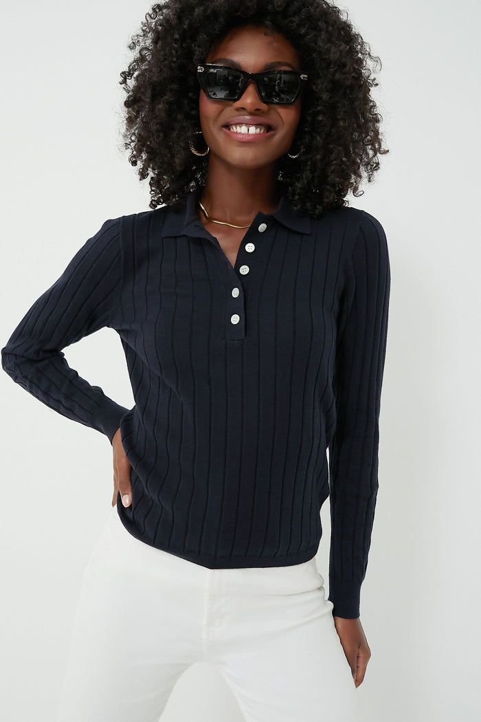 A woman in black sunglasses, white pants, and a navy Amanda Polo with ribbed texture and white buttons from Alex Mill stands smiling, showcasing timeless essentials.