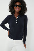 A woman in black sunglasses, white pants, and a navy Amanda Polo with ribbed texture and white buttons from Alex Mill stands smiling, showcasing timeless essentials.