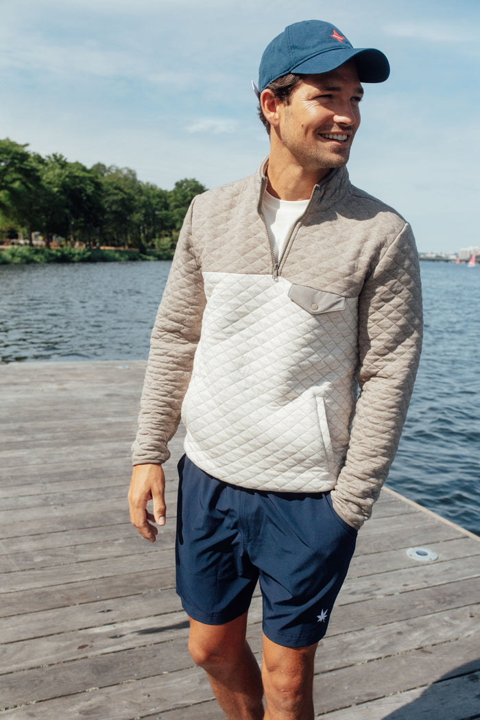 Young man on dock wearing the Navy Americana Tuckernuck Hat, a classic, effortlessly cool cotton cap with needlepoint embroidery and adjustable sailcloth strap, embodying fun, high-end style.