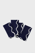 Four neatly folded Tuckernuck Home dark blue scalloped napkins with white wavy trim are arranged in a fanned-out pattern.