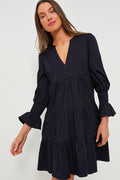 A woman wears a Pomander Place navy blue cotton poplin day dress with long sleeves, a V-neckline, ruffled cuffs, and a tiered skirt.