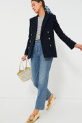 A person wears a Tuckernuck Navy Diana Blazer with gold buttons, a striped top, blue jeans, gold flats, and carries a woven handbag.