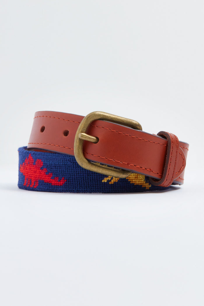 A brown leather belt with a brass buckle and navy needlepoint showing red and yellow dinosaurs, this Smathers and Branson dinosaur belt is perfect for children.