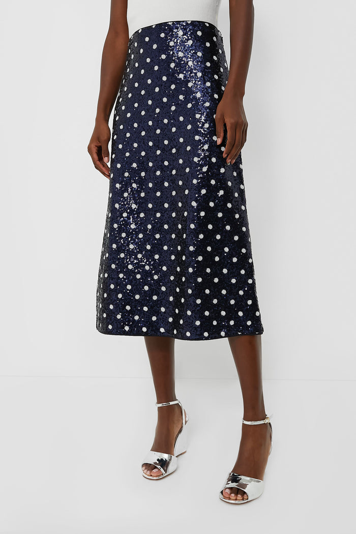 A person wears a Baum Und Pferdgarten Navy Dotted Sequence Jily Skirt with silver high-heeled sandals and a white sleeveless top.