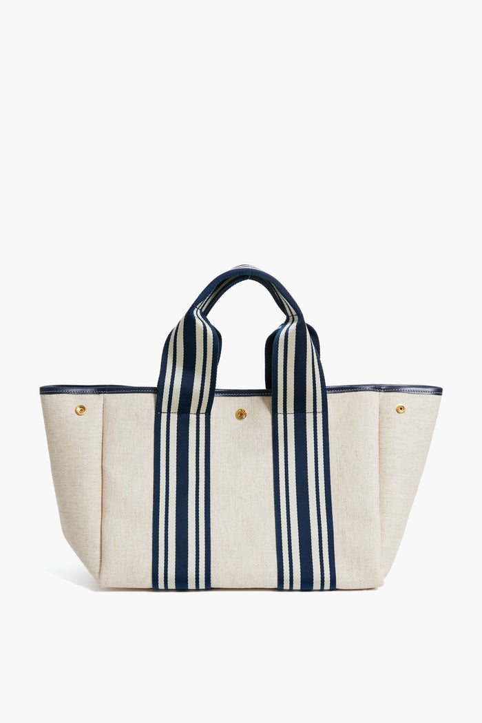 The Rue de Verneuil beige linen tote features navy striped handles, gold-tone buttons, and a structured rectangular shape, making it a stylish and versatile bag for daily essentials.