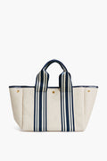 The Rue de Verneuil beige linen tote features navy striped handles, gold-tone buttons, and a structured rectangular shape, making it a stylish and versatile bag for daily essentials.