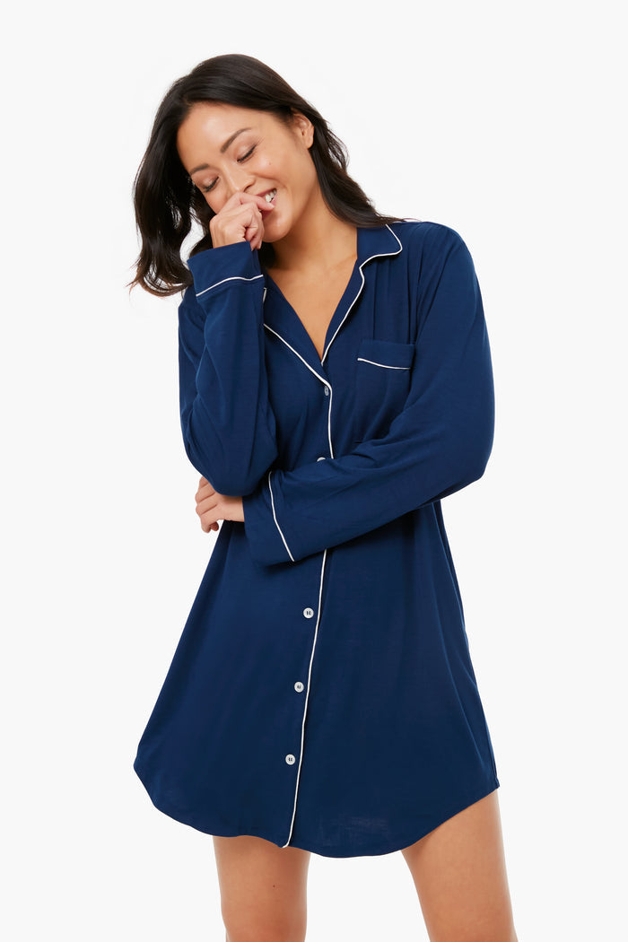 A person wearing an Eberjey navy blue nightshirt with white piping and buttons stands smiling with one hand near their face.
