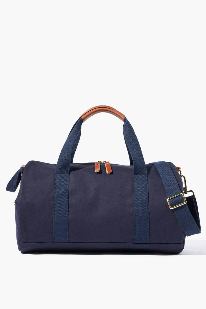 The Neely & Chloe navy blue gym duffel bag features dual handles, brown leather accents on the handles and zipper pulls, plus a detachable shoulder strap—an ideal blend of durability, function, and style for everyday use.