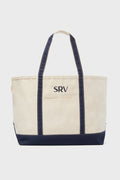 The CB Station beige canvas tote bag features navy blue handles, trim, and a custom SRV monogram embroidered on the front—ideal as a reusable everyday bag.