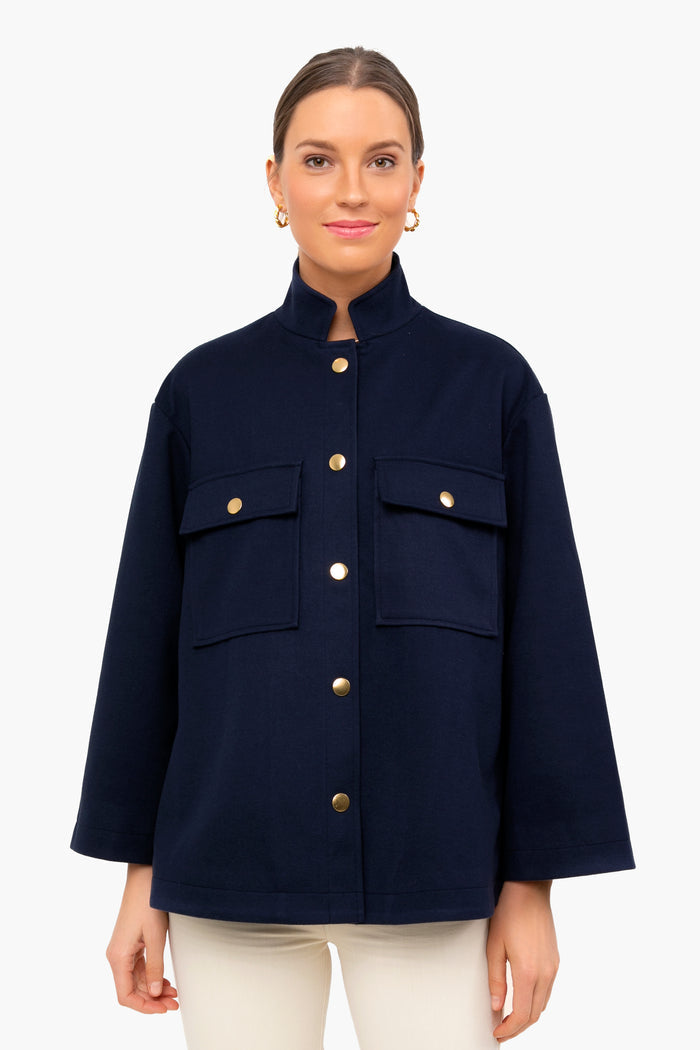 A woman wears a chic Navy Tuckernuck Shirt Jacket with large front pockets and gold buttons, paired with white pants for a minimalist look.