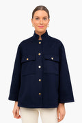 A woman wears a chic Navy Tuckernuck Shirt Jacket with large front pockets and gold buttons, paired with white pants for a minimalist look.