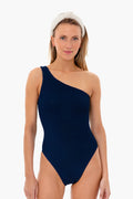 A woman stands confidently in a Hunza G navy blue one-shoulder, high-cut leg swimsuit with a white headband.