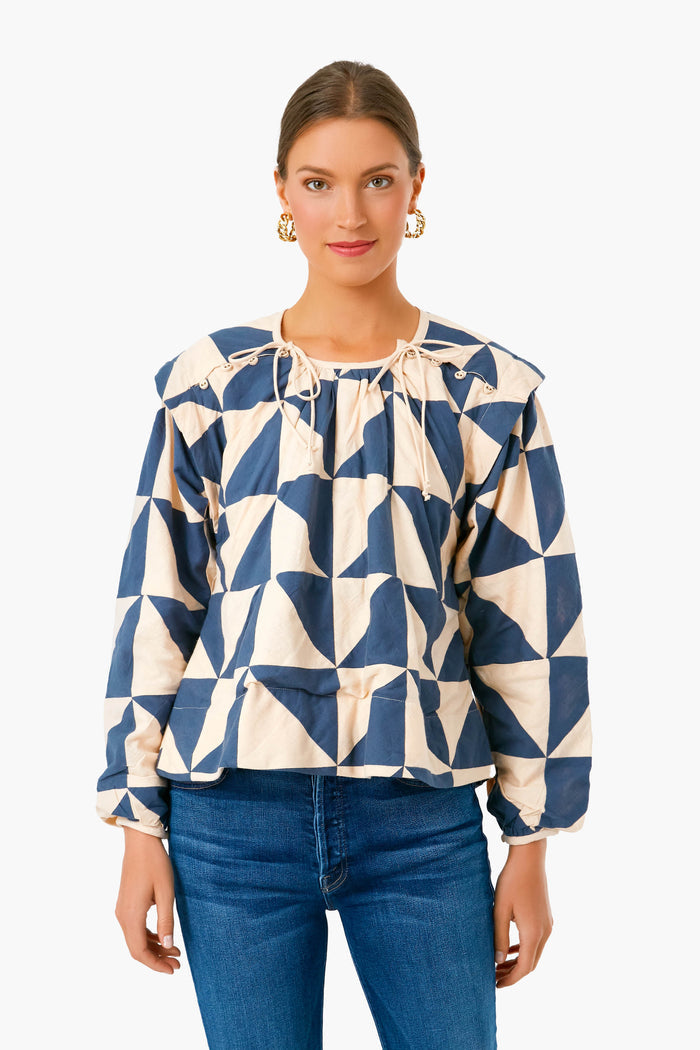 A woman wears a MIRTH blue and beige geometric long-sleeve tie-neck blouse with blue jeans, highlighting artisan-made clothing in an effortlessly chic style.