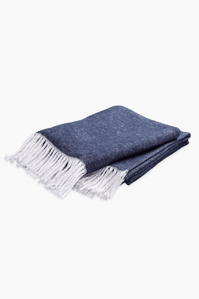 Classic Navy Pezzo Throw with white fringe, crafted from soft cotton. This high-end, effortless piece is perfect for adding cozy, fun elegance to any space.