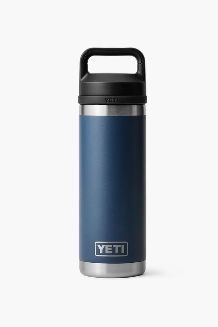 A YETI Rambler Bottle in navy blue stainless steel with double-wall vacuum insulation and a black handle lid, shown standing upright.