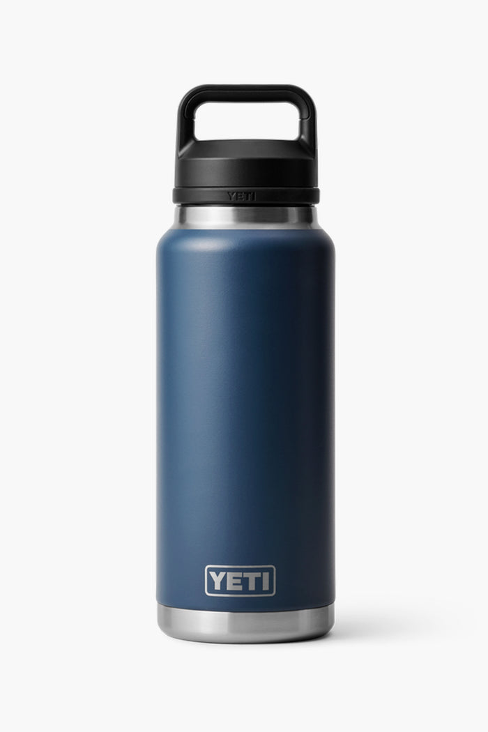 A YETI Rambler 36oz Bottle in navy blue with a black handle lid stands upright. Its durable stainless steel build keeps drinks cold for hours.