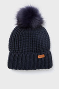 A chunky-knit navy blue Barbour beanie featuring a large faux-fur pom-pom on top and a small brown Barbour logo patch on the front cuff.