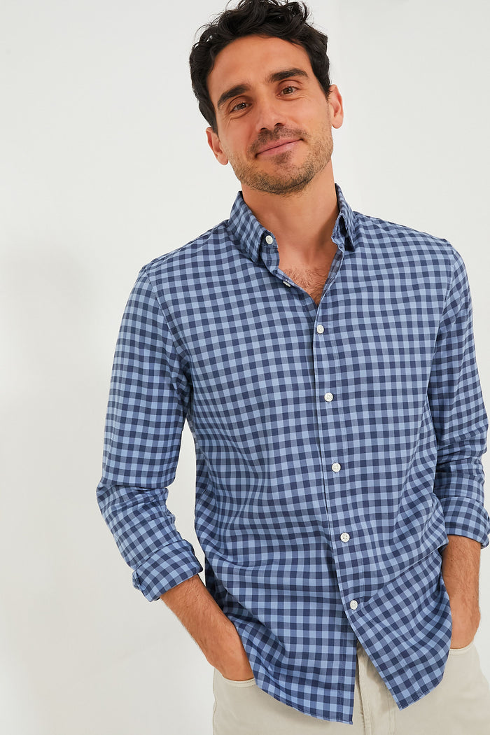 A man wearing a blue and white checkered Faherty wrinkle-free shirt and beige pants stands with his hands in his pockets, showcasing sustainable apparel.