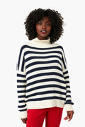 A woman stands facing forward wearing an Emerson Fry navy stripe funnel neck sweater and red pants.