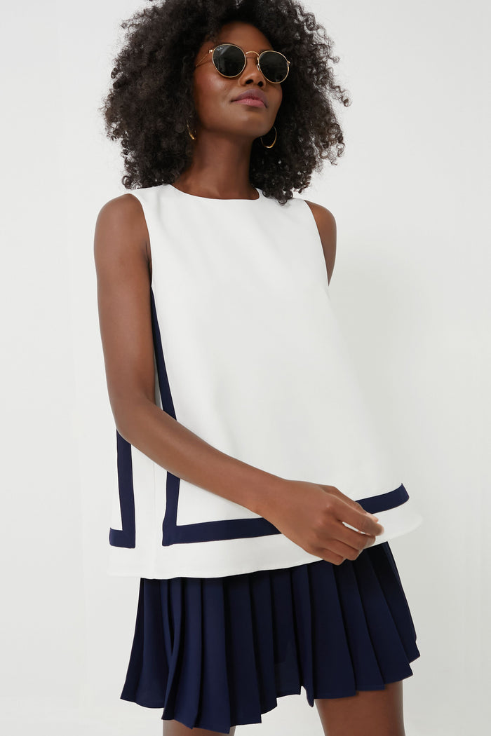 A woman wearing sunglasses and a Tuckernuck Navy Stripe Tyler Top with navy trim, paired with a pleated navy skirt.