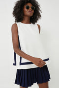 A woman wearing sunglasses and a Tuckernuck Navy Stripe Tyler Top with navy trim, paired with a pleated navy skirt.