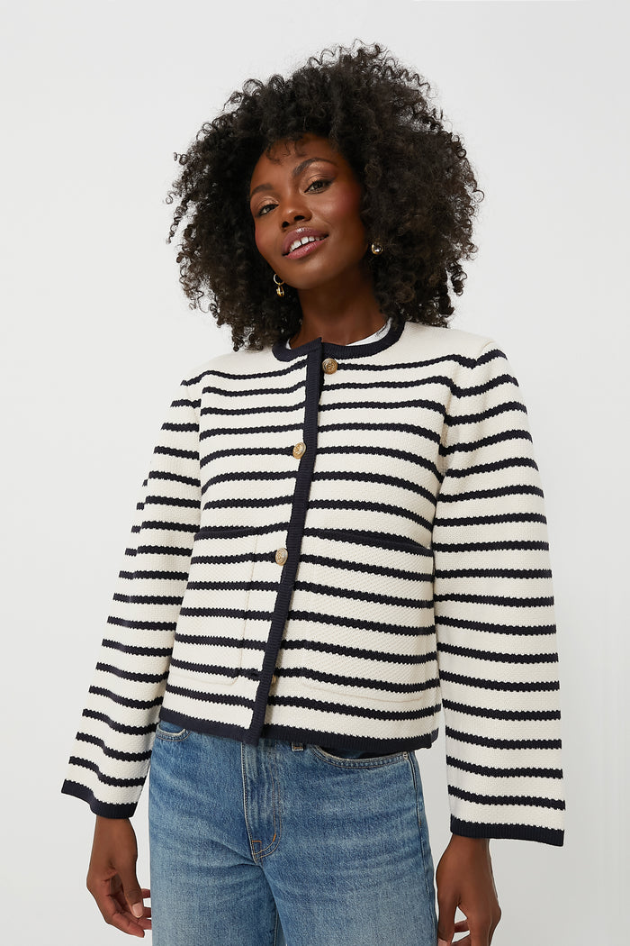 A person wears a Moon River white and black striped cardigan with gold buttons and blue jeans, featuring a cropped hem.