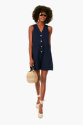 Woman wearing a sleeveless Navy Myla Romper by Pomander Place with front buttons, sunglasses, wedge heels, and holding a round straw handbag.
