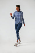 A woman in a Tnuck Sport navy trellis gingham long sleeve top and matching side-detailed leggings pairs her look with gray sneakers as she walks confidently.