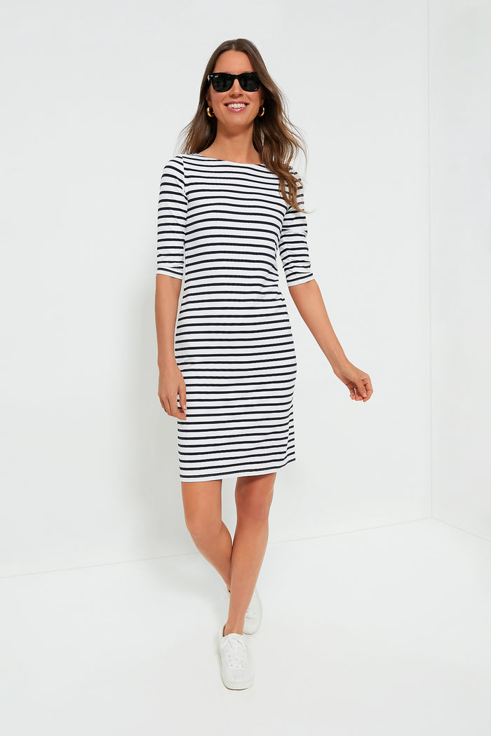 A woman in sunglasses and a Saint James black-and-white striped dress with elbow-length sleeves and white sneakers stands confidently, showcasing classic style.