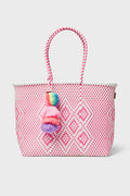 The Squeeze de Citron tote is a pink and white Mexican artisan bag, handmade from recycled plastic with a diamond pattern, two handles, and a multicolored pom-pom tassel.