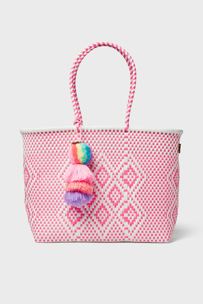 The Squeeze de Citron tote is a pink and white Mexican artisan bag, handmade from recycled plastic with a diamond pattern, two handles, and a multicolored pom-pom tassel.